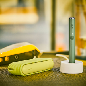 An IQOS ILUMA device in a charging station with a Pocket Charger on a table.